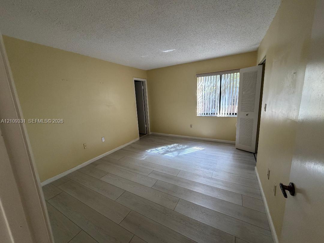 Interior space featuring wood-finish tile flooring, a window with vertical blinds, and a built-in closet with louvered doors