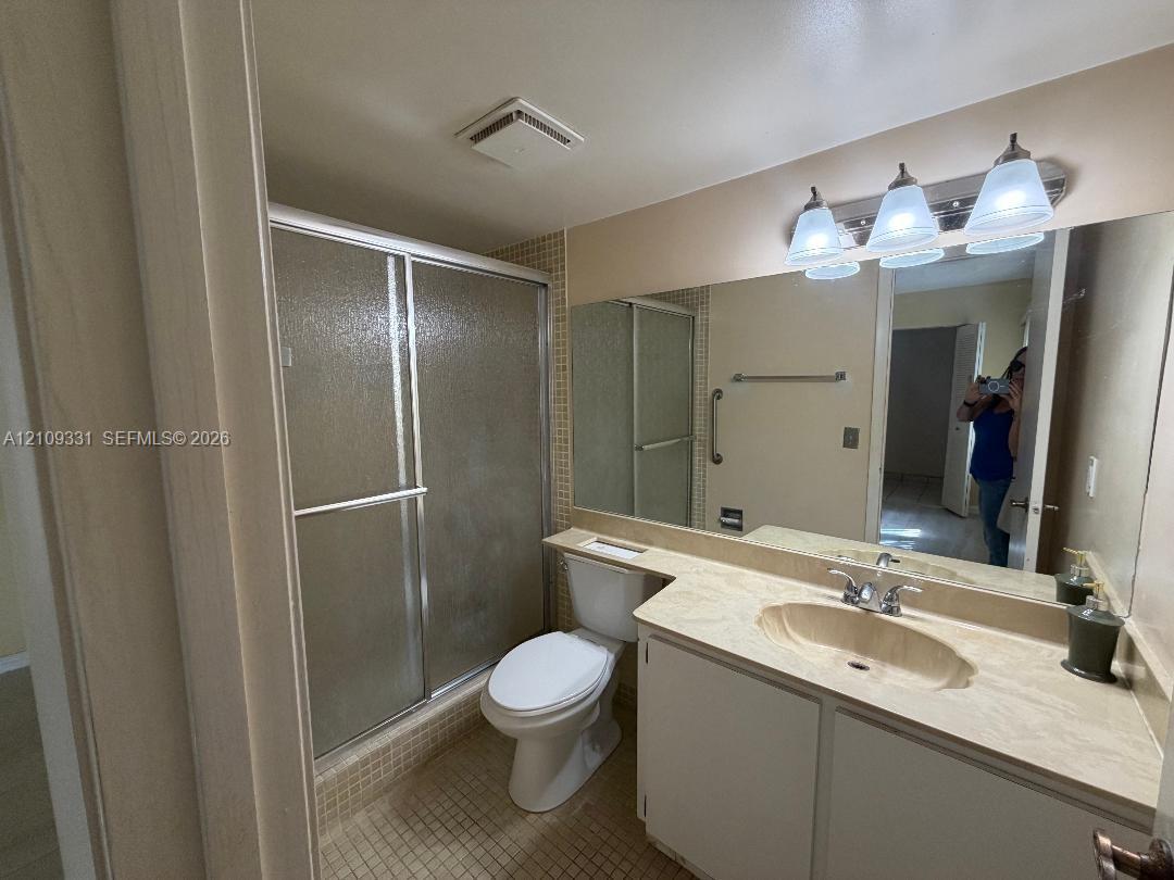 Bathroom featuring a glass-enclosed shower, stone-surfaced vanity with an integrated oval sink, and a full-width vanity mirror with integrated three-bulb lighting