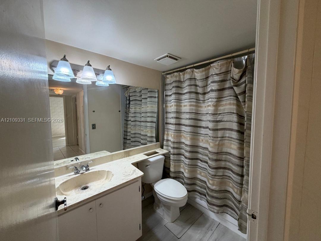 Bathroom vanity with stone-finish countertop, integrated sink, large wall-mounted mirror, three-light fixture, and wood-finish flooring
