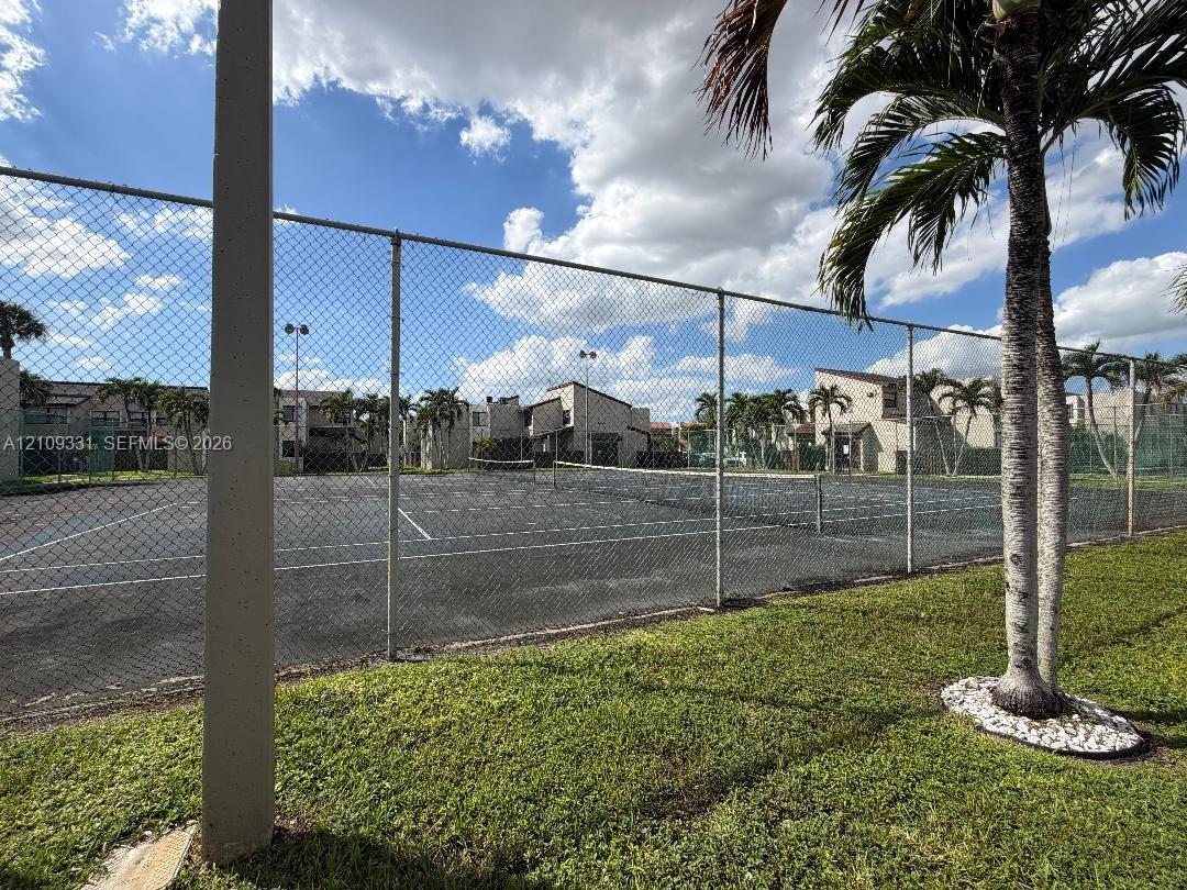Tennis court with a chain-link perimeter fence, integrated lighting, and manicured landscaping