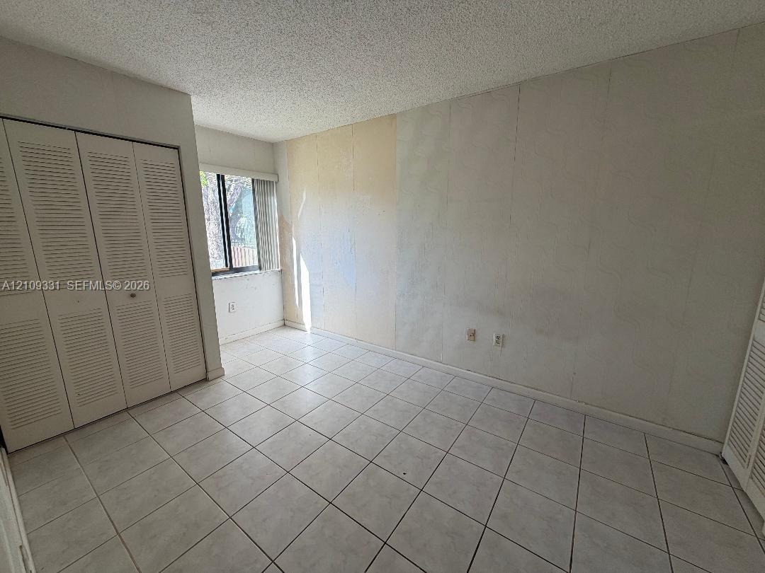 Room featuring white tile flooring, dual louvered-door closets, and a window with vertical blinds