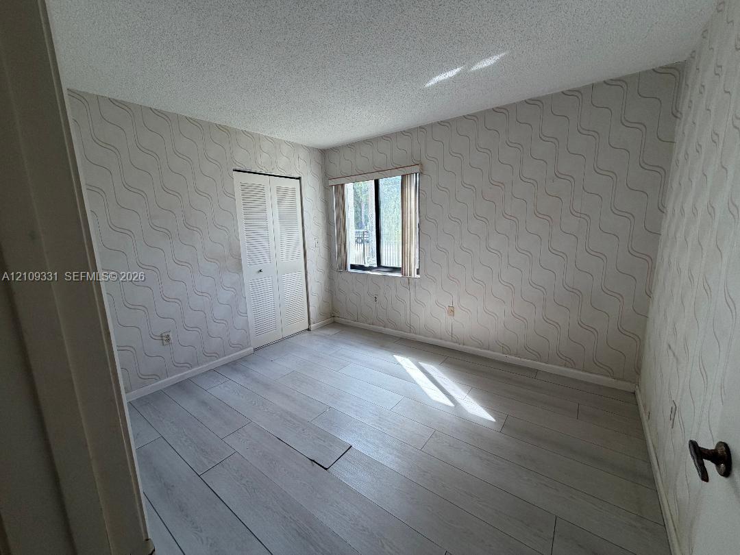 Room featuring wood-finish flooring, textured wallpaper, a single window, and dual-panel closet doors