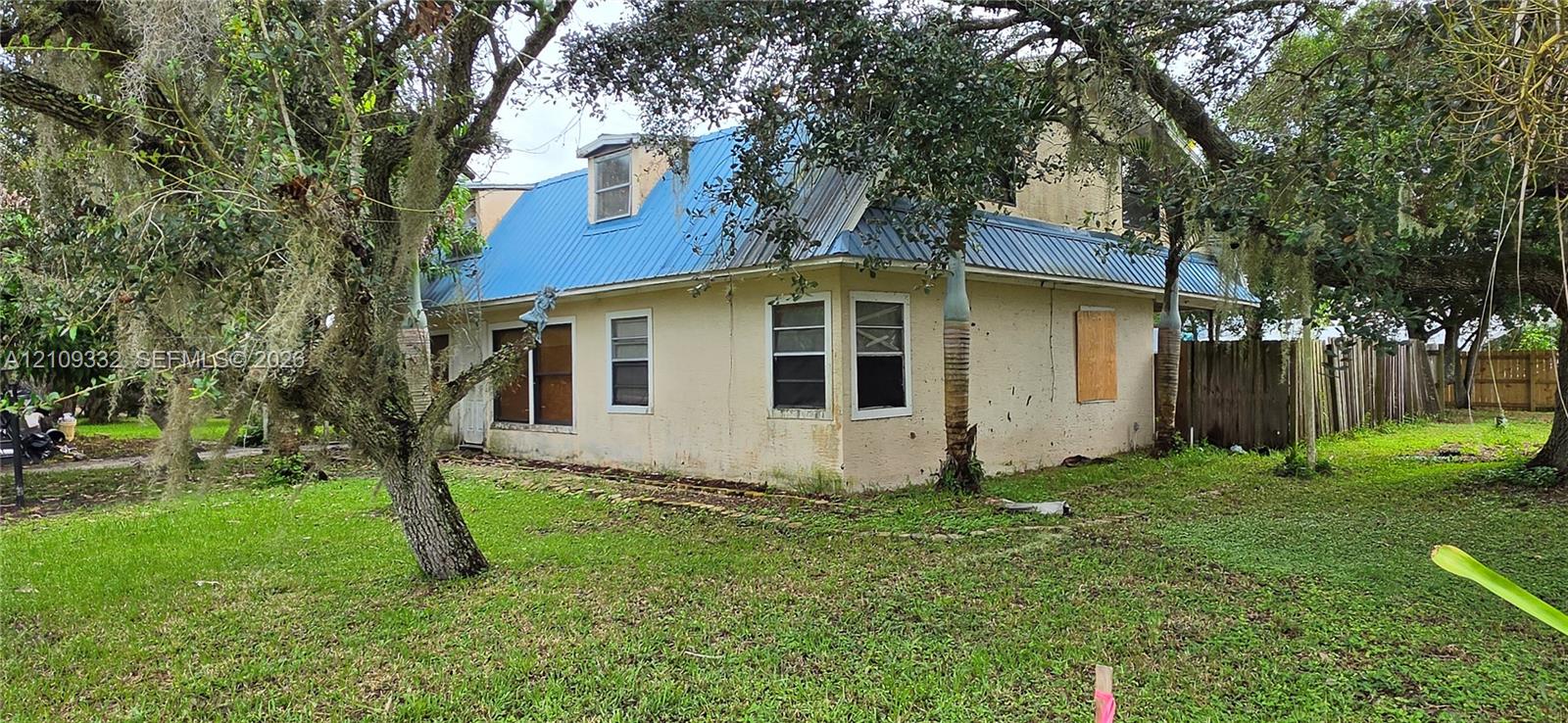 Stucco exterior residence featuring a blue metal roof, dormer windows, and a wood privacy fence