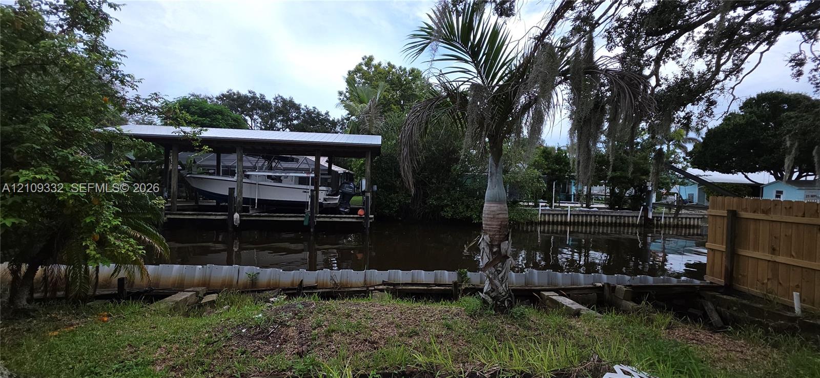 Waterfront property featuring a private covered boat lift, bulkhead seawall, and mature tropical landscaping