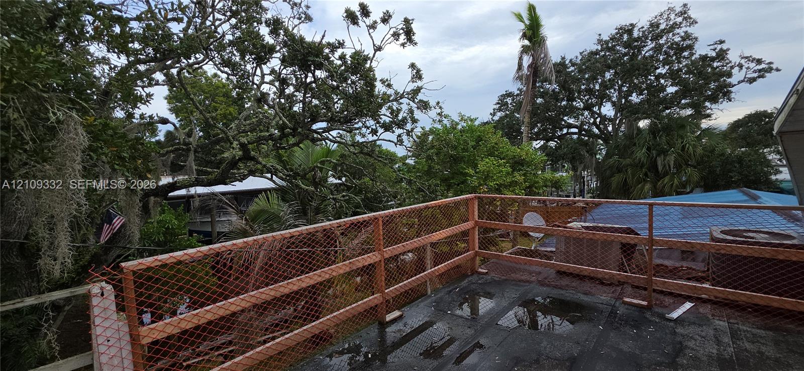 Elevated wooden deck featuring metal mesh railing and surrounding mature trees