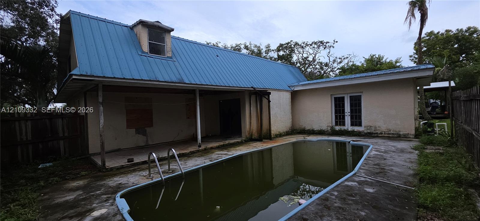 In-ground swimming pool with metal ladder, covered patio area, and dual-pane glass French doors