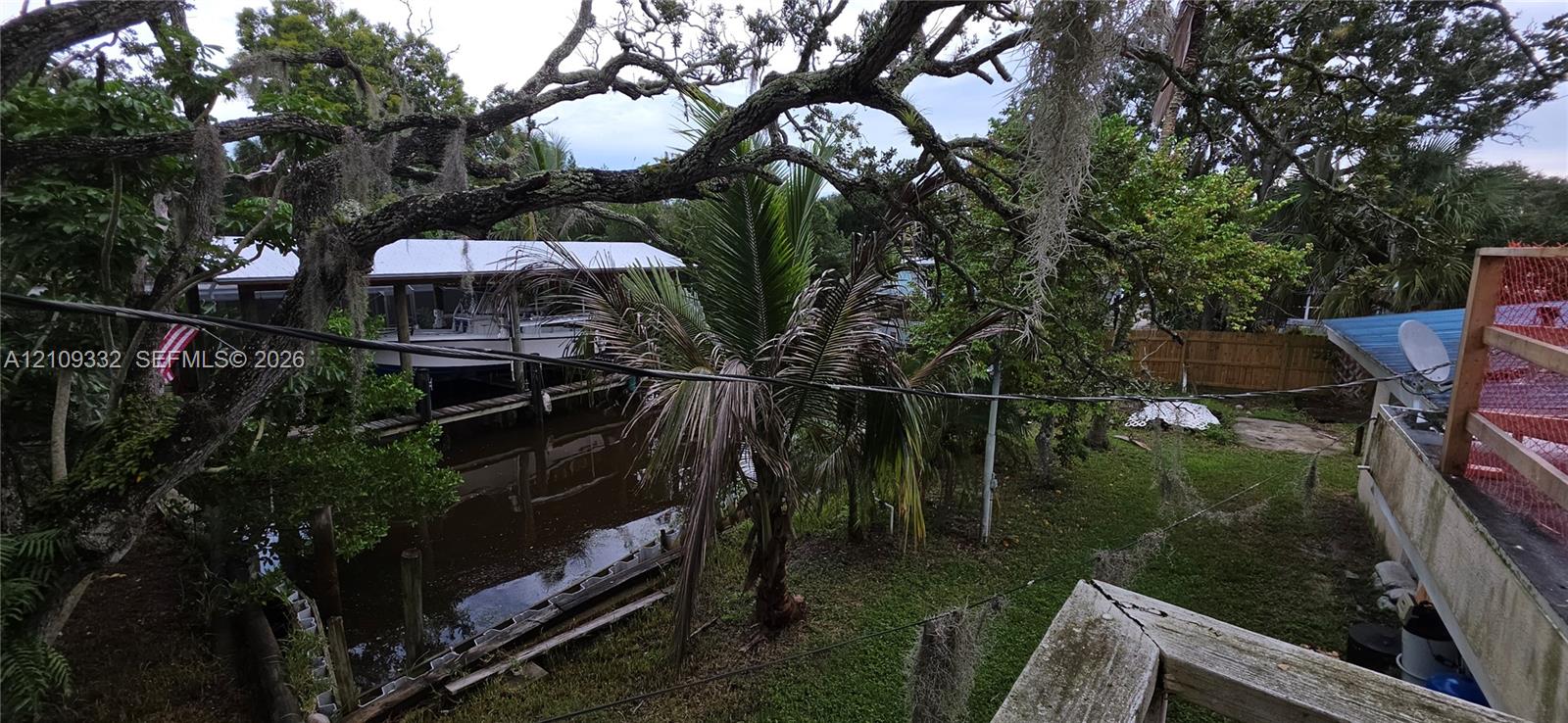 Canal-front property featuring a private boat dock, mature oak trees, tropical landscaping, and a fenced perimeter