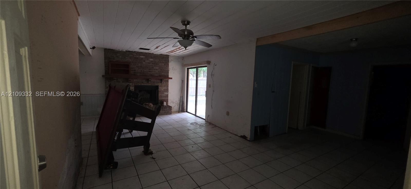 Interior space featuring tile flooring, a floor-to-ceiling brick fireplace with a wood mantel, a plank-style ceiling with an integrated fan, and a sliding glass door