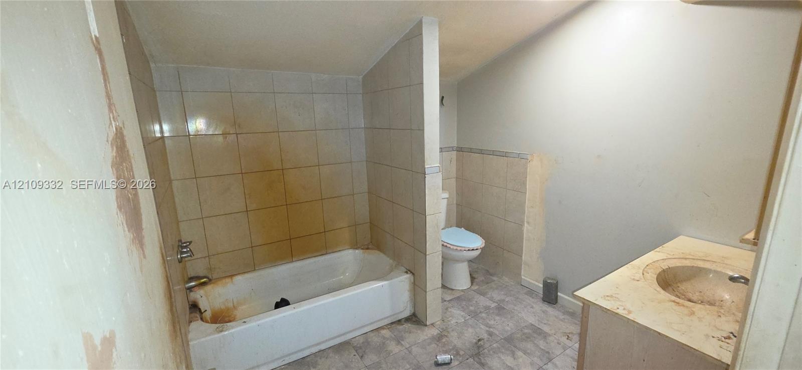 Bathroom featuring a bathtub, tile surround, vanity with an integrated basin, and toilet