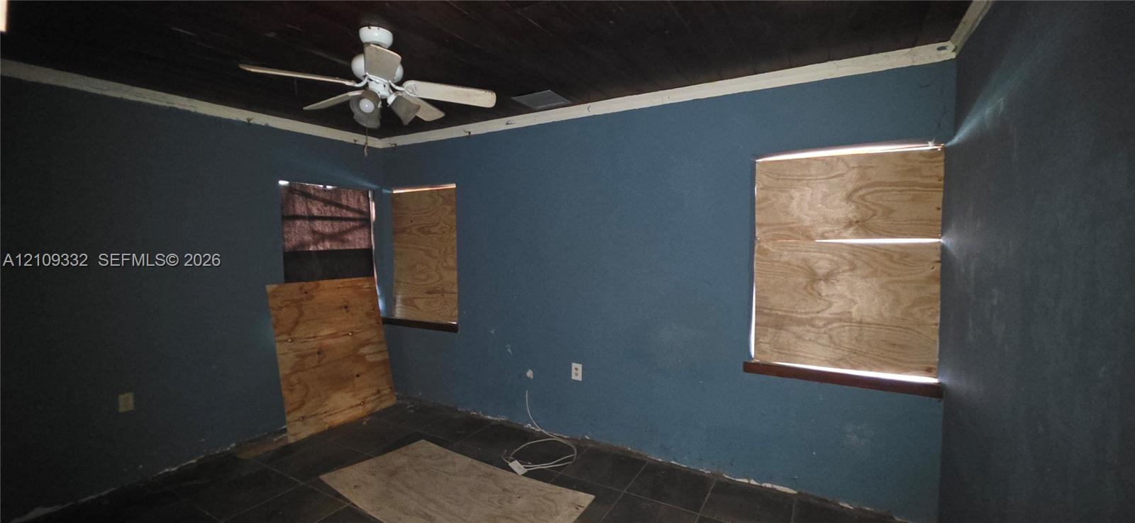 Dark-toned wood plank ceiling, dual-tone wall finish, and large-format floor tiling featuring a mounted ceiling fan