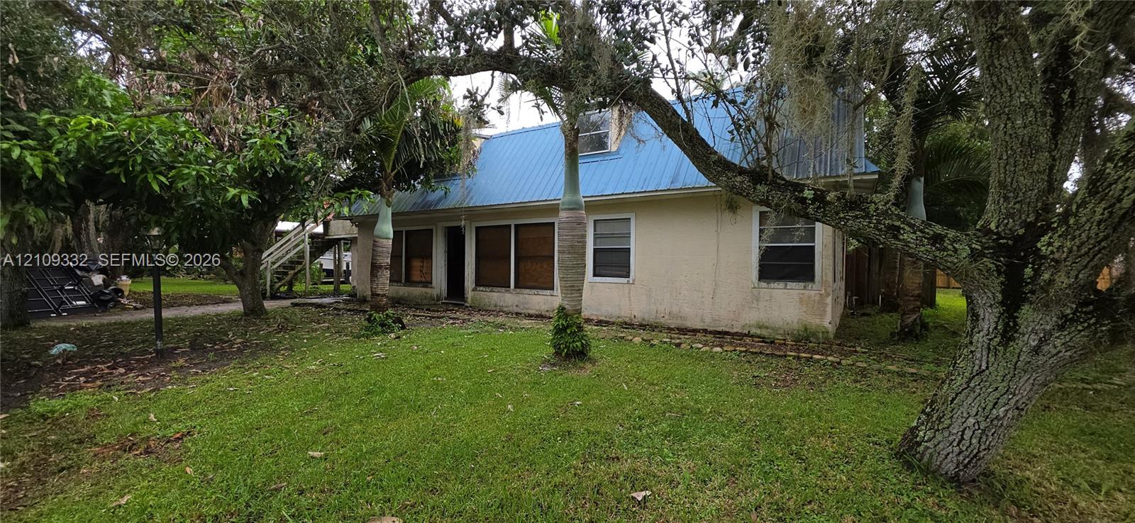 Stucco exterior residence featuring a blue metal roof, grass lawn, and mature canopy trees