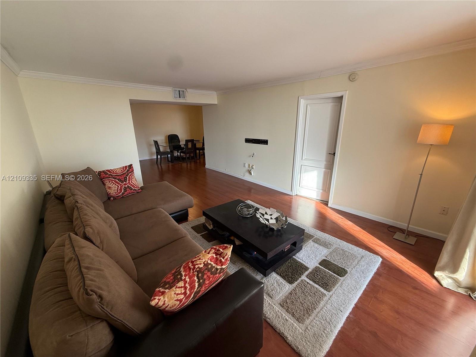 Wood-finish flooring, neutral wall tones, crown molding, and a single-panel interior door Wood-finish flooring, neutral wall tones, crown molding, and a single-panel interior door