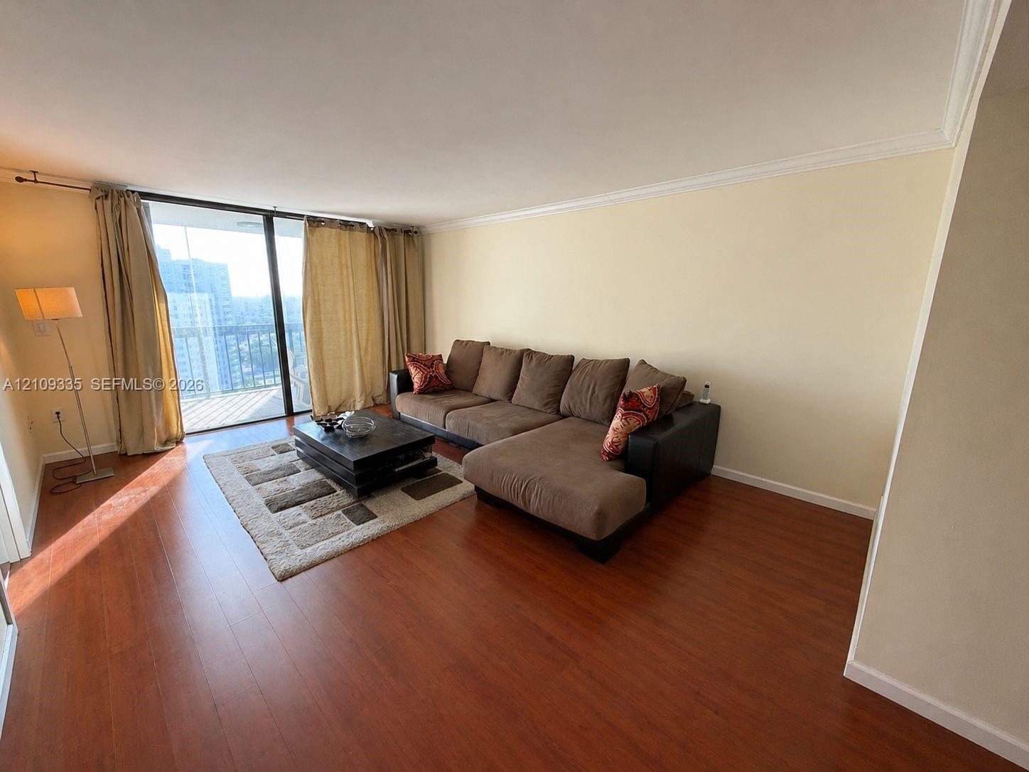 Living area featuring wood-finish flooring, crown molding, and sliding glass doors leading to an exterior balcony Living area featuring wood-finish flooring, crown molding, and sliding glass doors leading to an exterior balcony