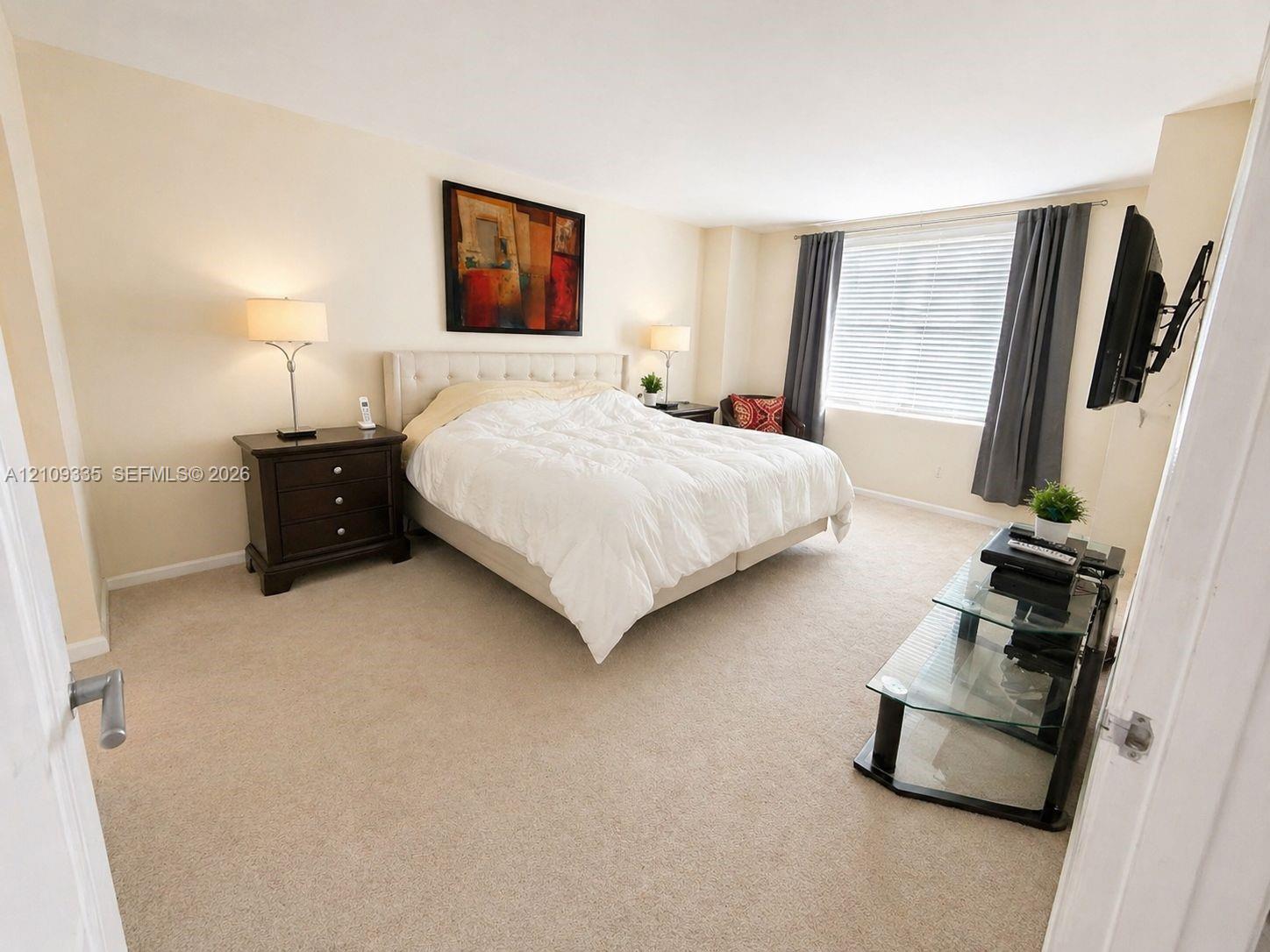 Neutral-toned interior space featuring wall-to-wall carpeting and a window with horizontal blinds Neutral-toned interior space featuring wall-to-wall carpeting and a window with horizontal blinds