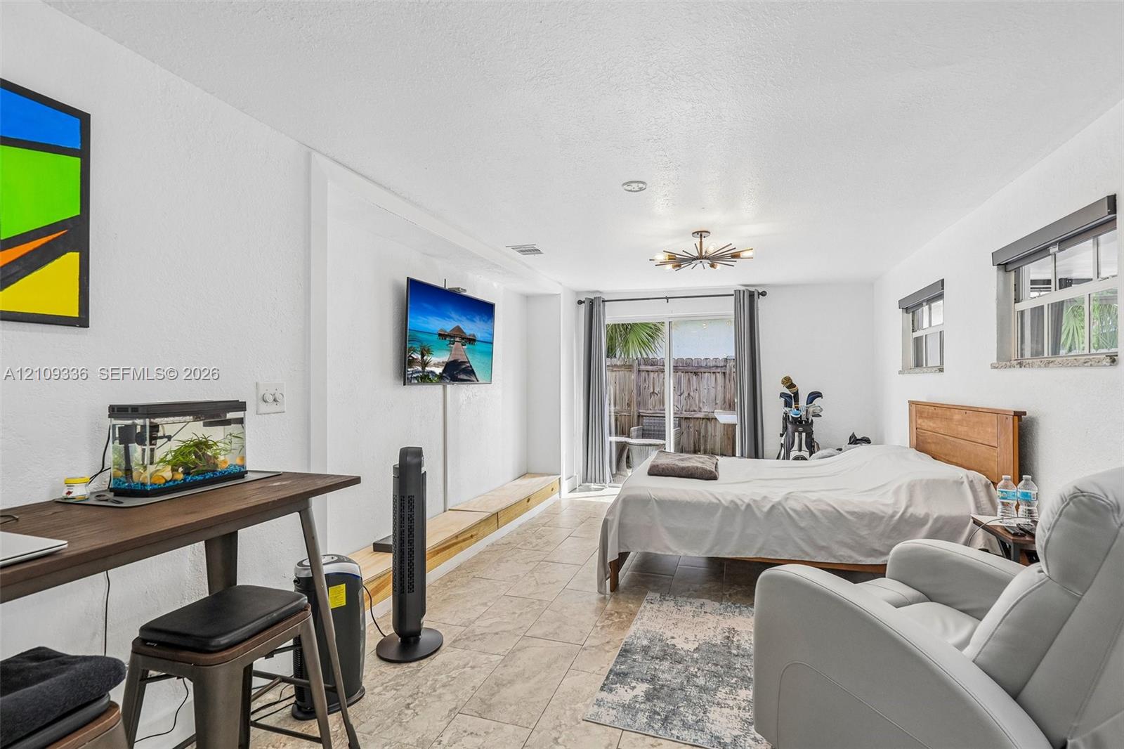 Room featuring stone-finish tile flooring, a wall-mounted television, a built-in low-profile wooden media console, a multi-arm flush-mount light fixture, and sliding glass doors