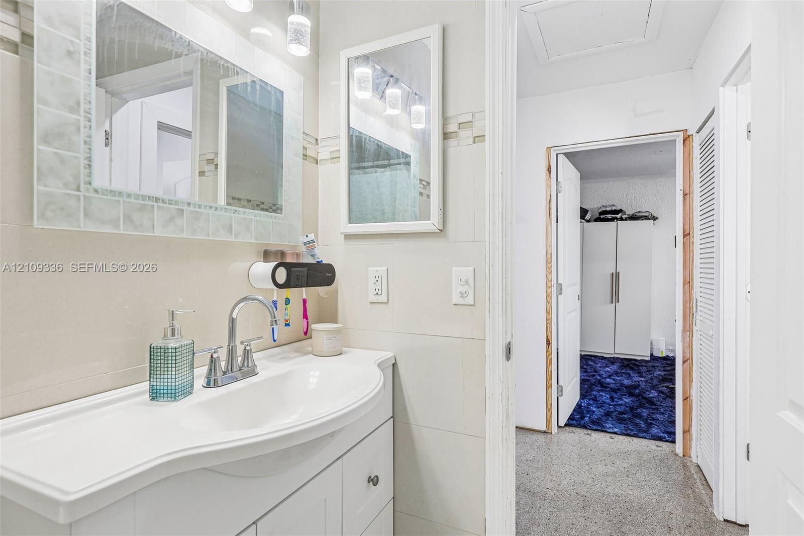 Bathroom vanity featuring an integrated basin, chrome faucet, wall-mounted mirror, and decorative tile backsplash