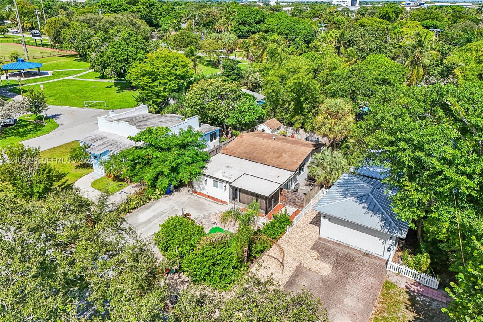 Aerial perspective featuring a detached garage with a metal roof, a screened-in porch, paved driveway space, and mature perimeter landscaping