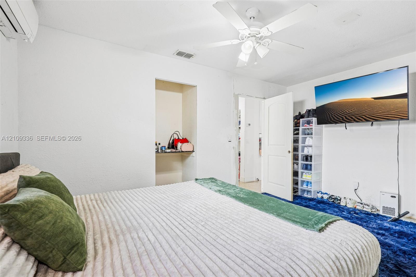 Wall-mounted mini-split HVAC unit, ceiling fan with integrated lighting, and an arched-top interior door