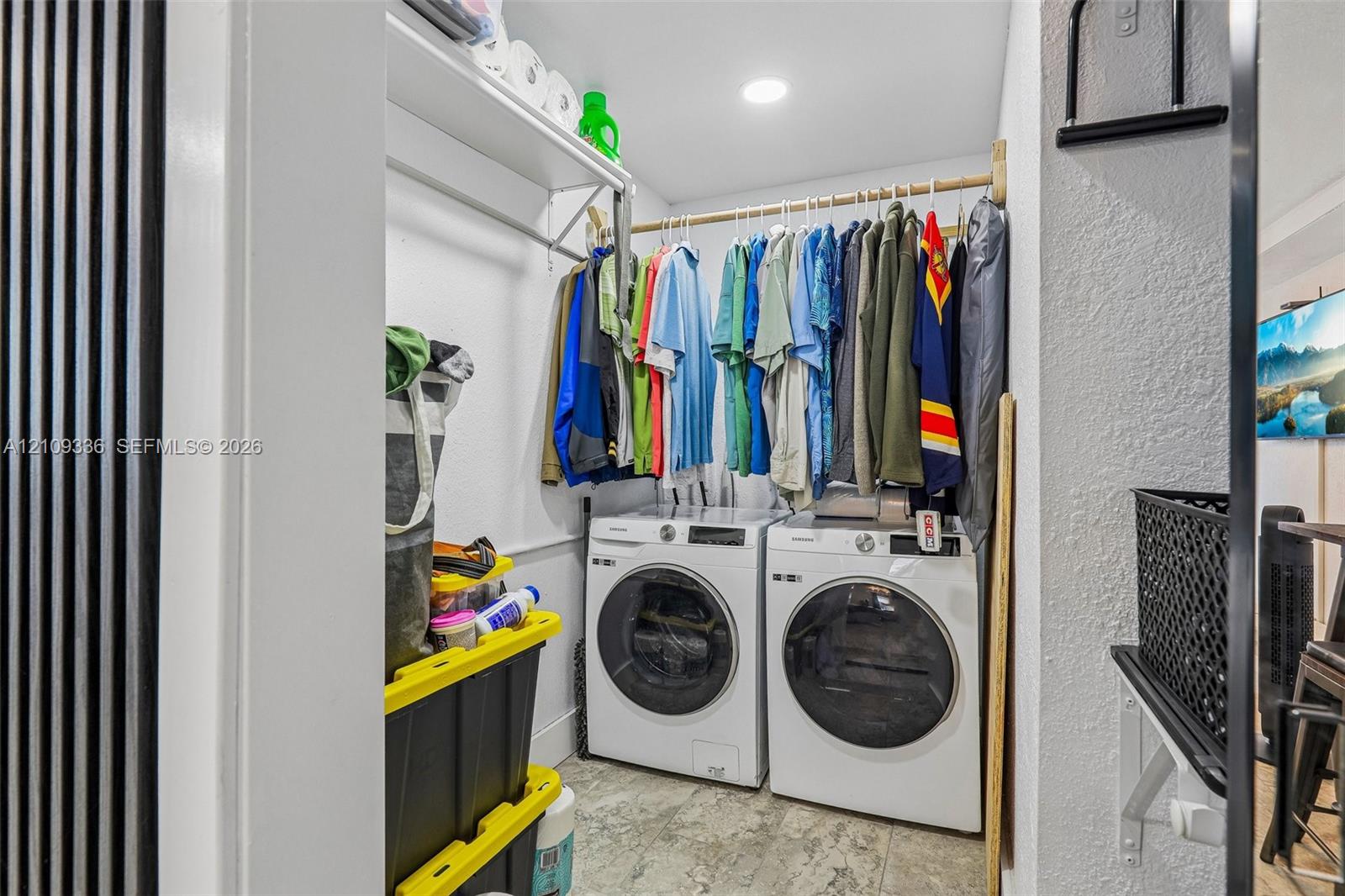Laundry area featuring white front-loading washer and dryer, integrated overhead shelving, a dedicated garment rod, and tile flooring