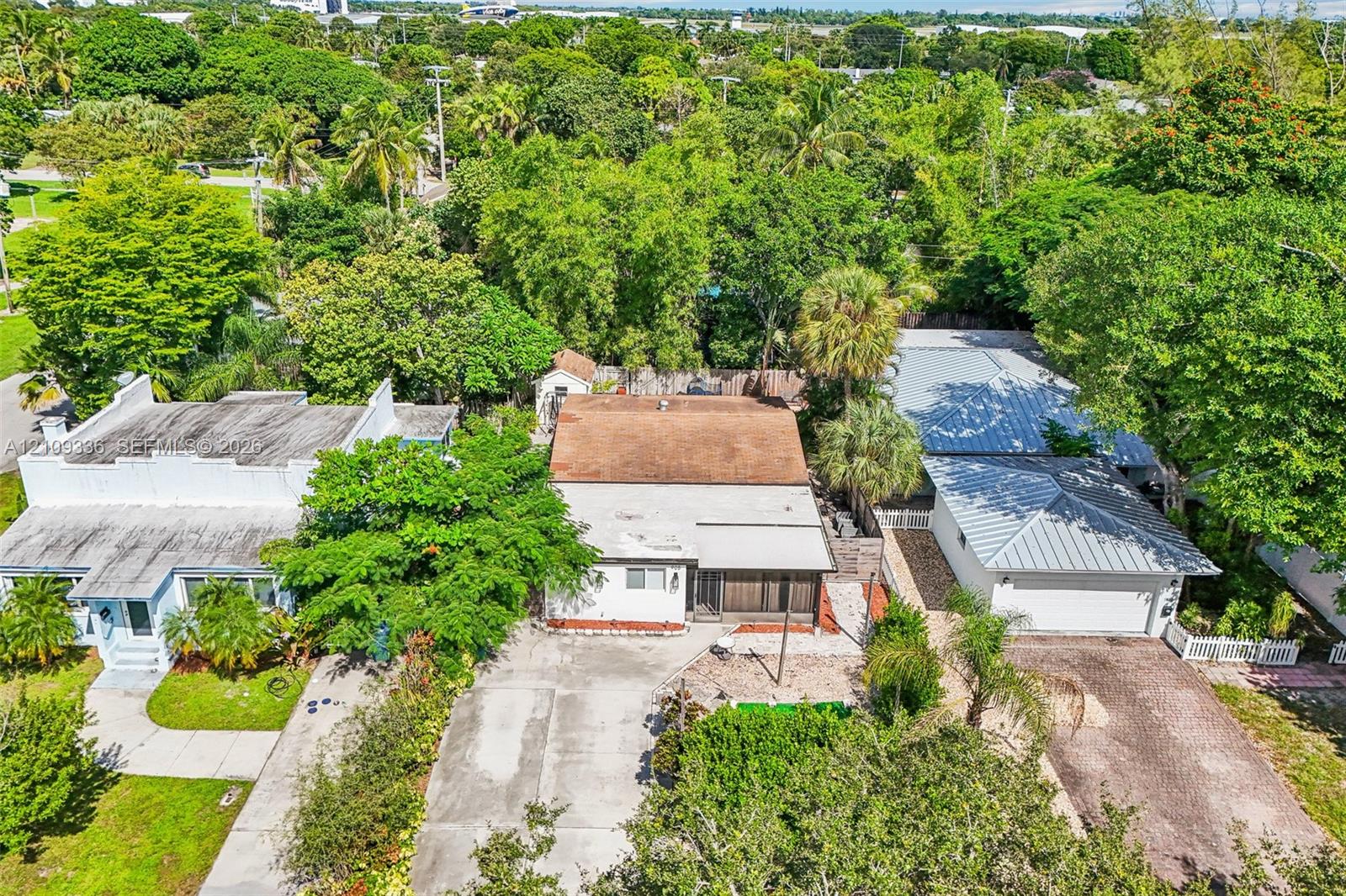 Aerial perspective of a multi-structure residential property featuring mature trees, paved driveways, a metal roof, and stone-finished exterior detailing