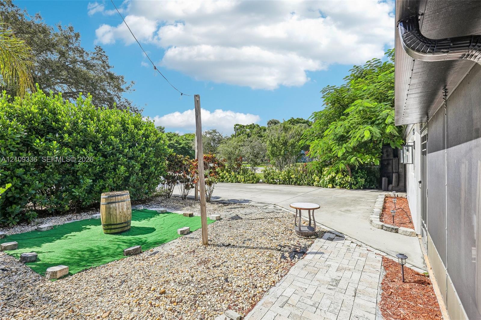 Outdoor space featuring a paved walkway, gravel ground cover, and mature perimeter landscaping
