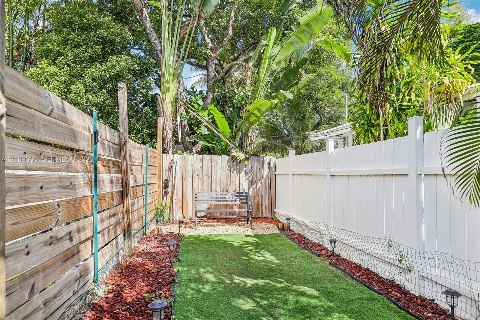 Outdoor area featuring a synthetic turf lawn, wood-slat privacy fencing, vinyl privacy fencing, and stone-accented ground cover