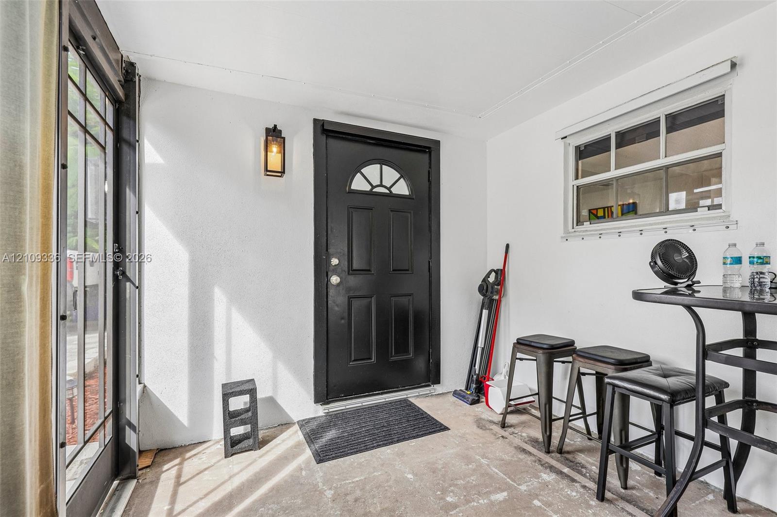 Covered entry featuring a black multi-panel door with arched window detail, a wall-mounted exterior lantern, and a multi-pane horizontal window