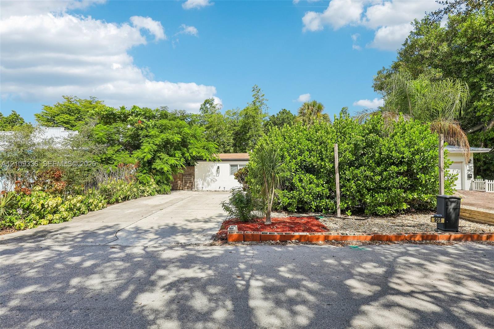 Concrete driveway, mature landscaping, and red mulch garden beds