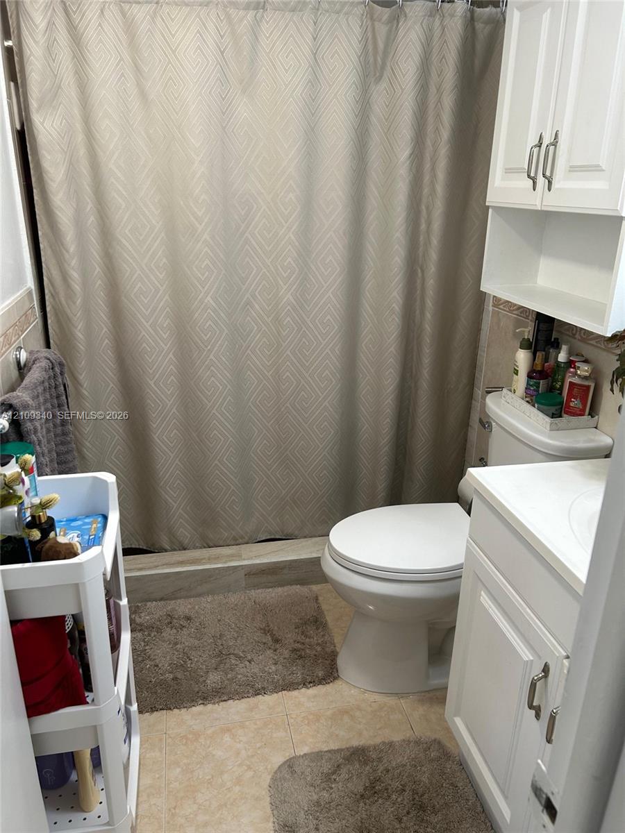 Bathroom featuring a tub-shower combination with tiled surround, white vanity cabinet, matching wall-mounted storage cabinetry, and hard-surface flooring