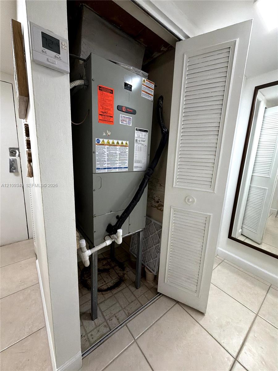 Utility closet containing a central heating and cooling unit with louvered bi-fold door access and programmable digital wall-mounted thermostat