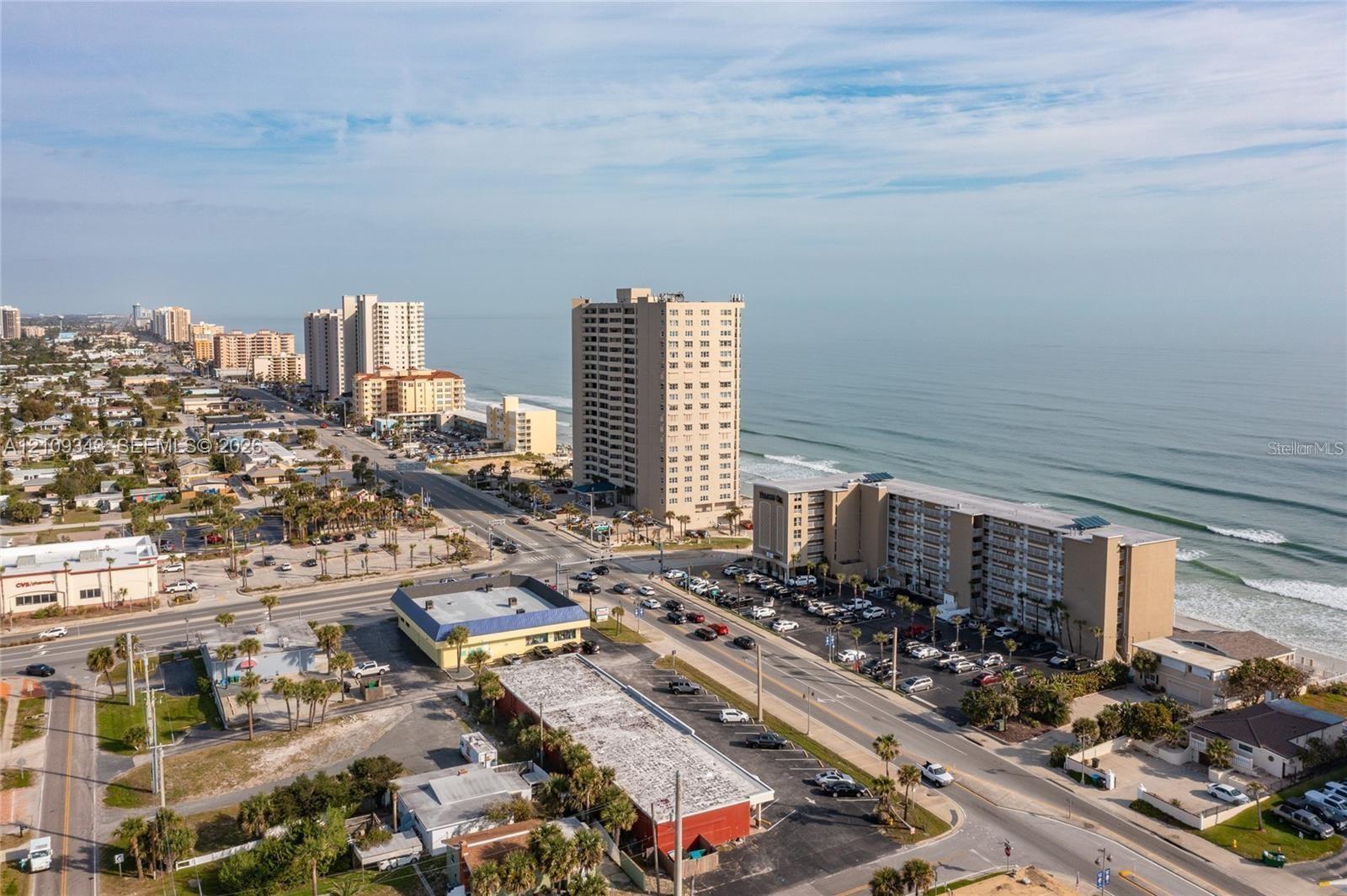 Aerial perspective of coastal landscape featuring direct oceanfront positioning, expansive sandy shoreline, and proximity to major roadways