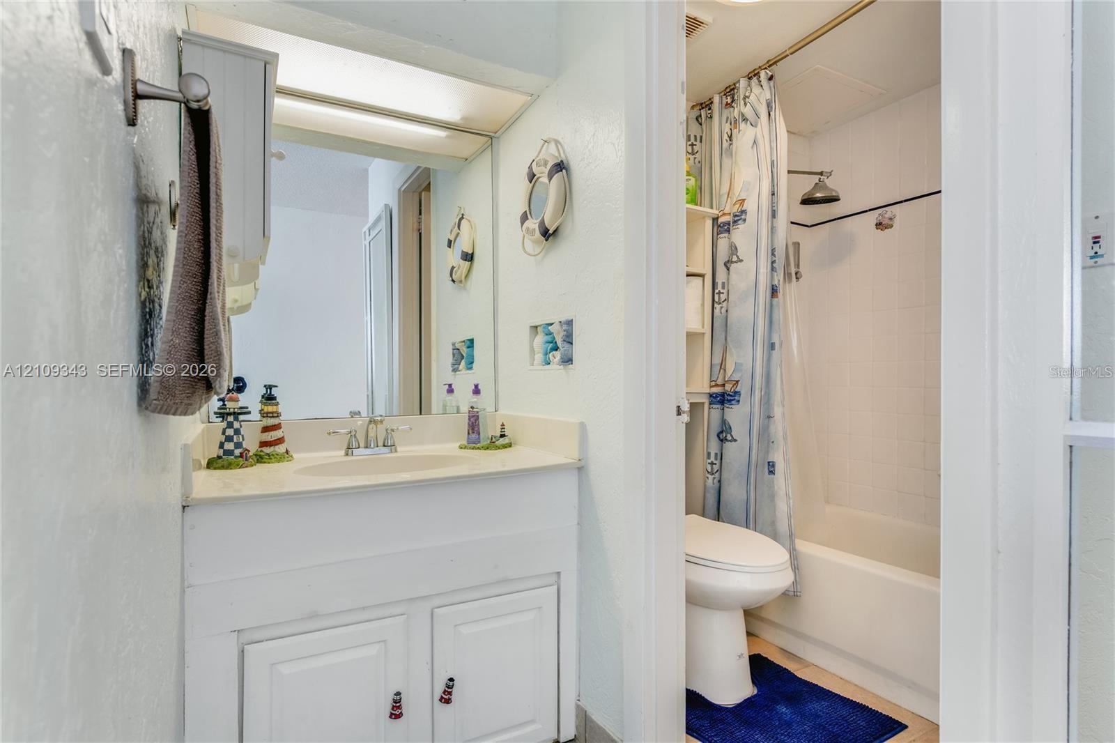 Bathroom featuring a white vanity with an integrated sink, dual-handle faucet, large wall-mounted mirror, and a tub-shower combination with a fixed showerhead