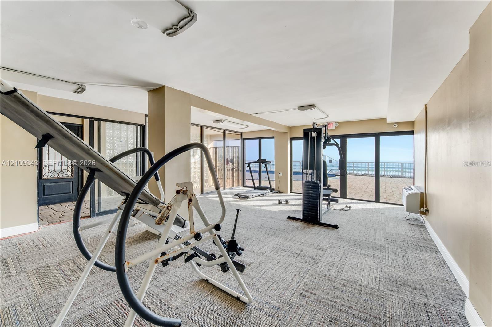 Multi-purpose room featuring modular carpet tile flooring, expansive floor-to-ceiling glass panel walls, and sliding glass doors with direct exterior access
