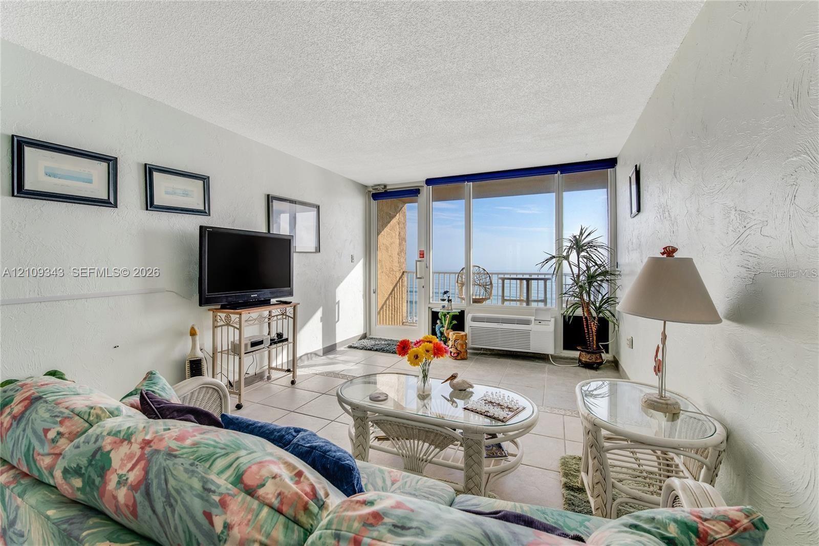 Living area featuring neutral tile flooring, expansive floor-to-ceiling windows, and access to an exterior balcony