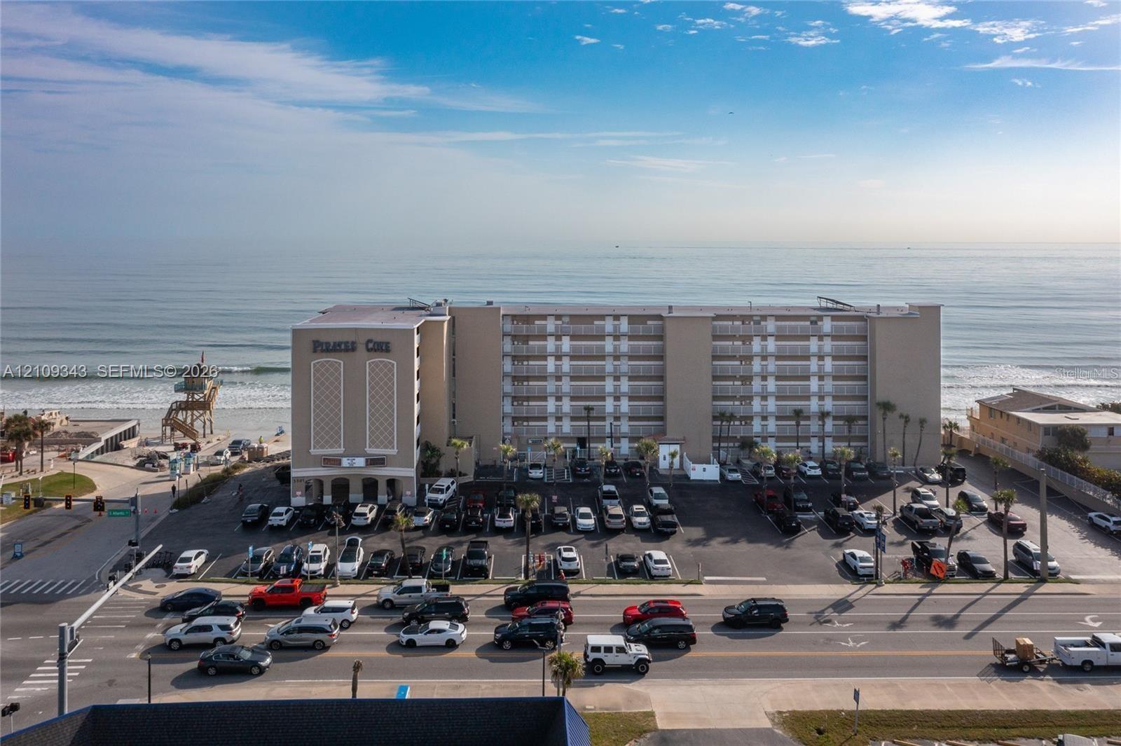Multi-story coastal condominium complex featuring private balconies, paved surface parking, and direct oceanfront positioning