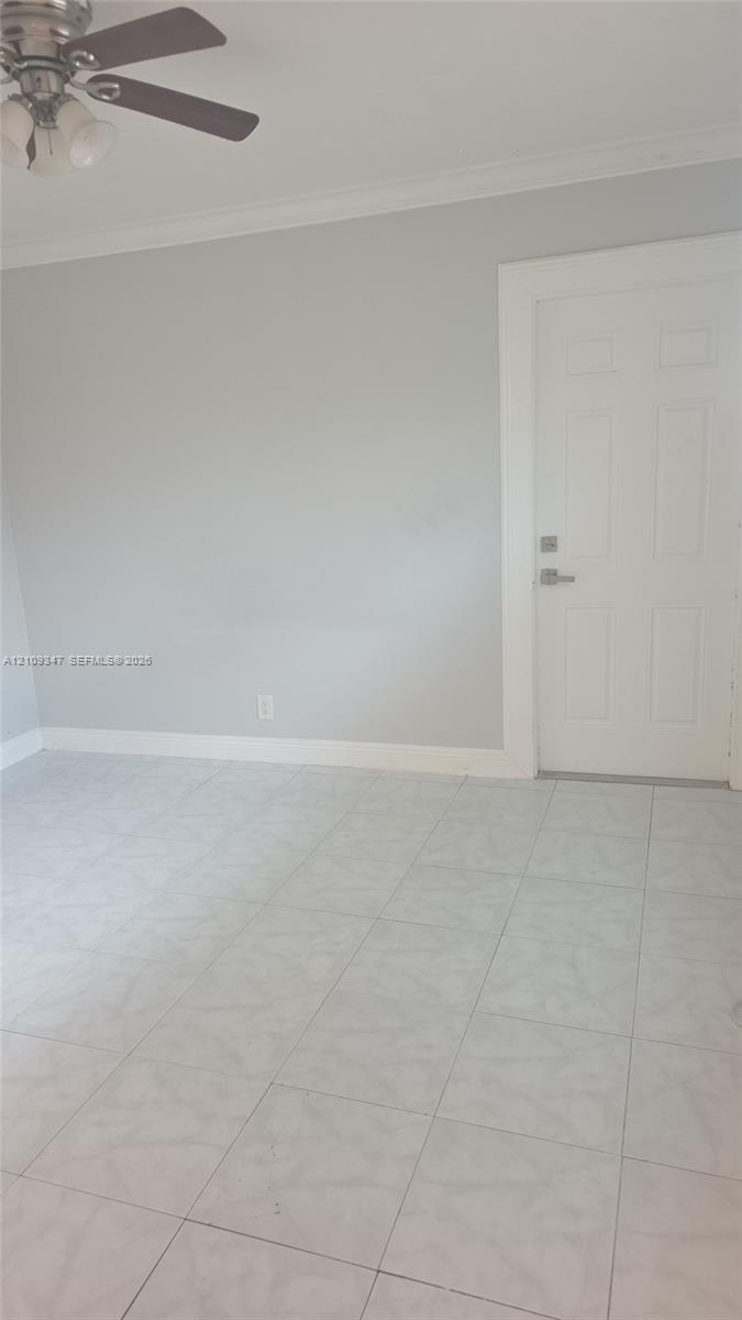 Neutral-toned interior space featuring tile flooring, crown molding, and a multi-paneled door with brushed metal hardware, complemented by an overhead ceiling fan with attached lighting