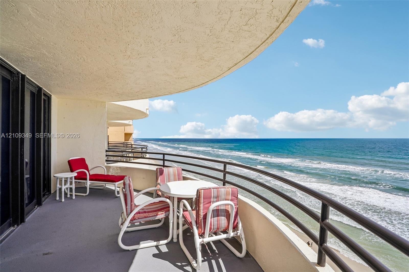 Curved covered balcony with a concrete floor, metal railings, and direct ocean exposure