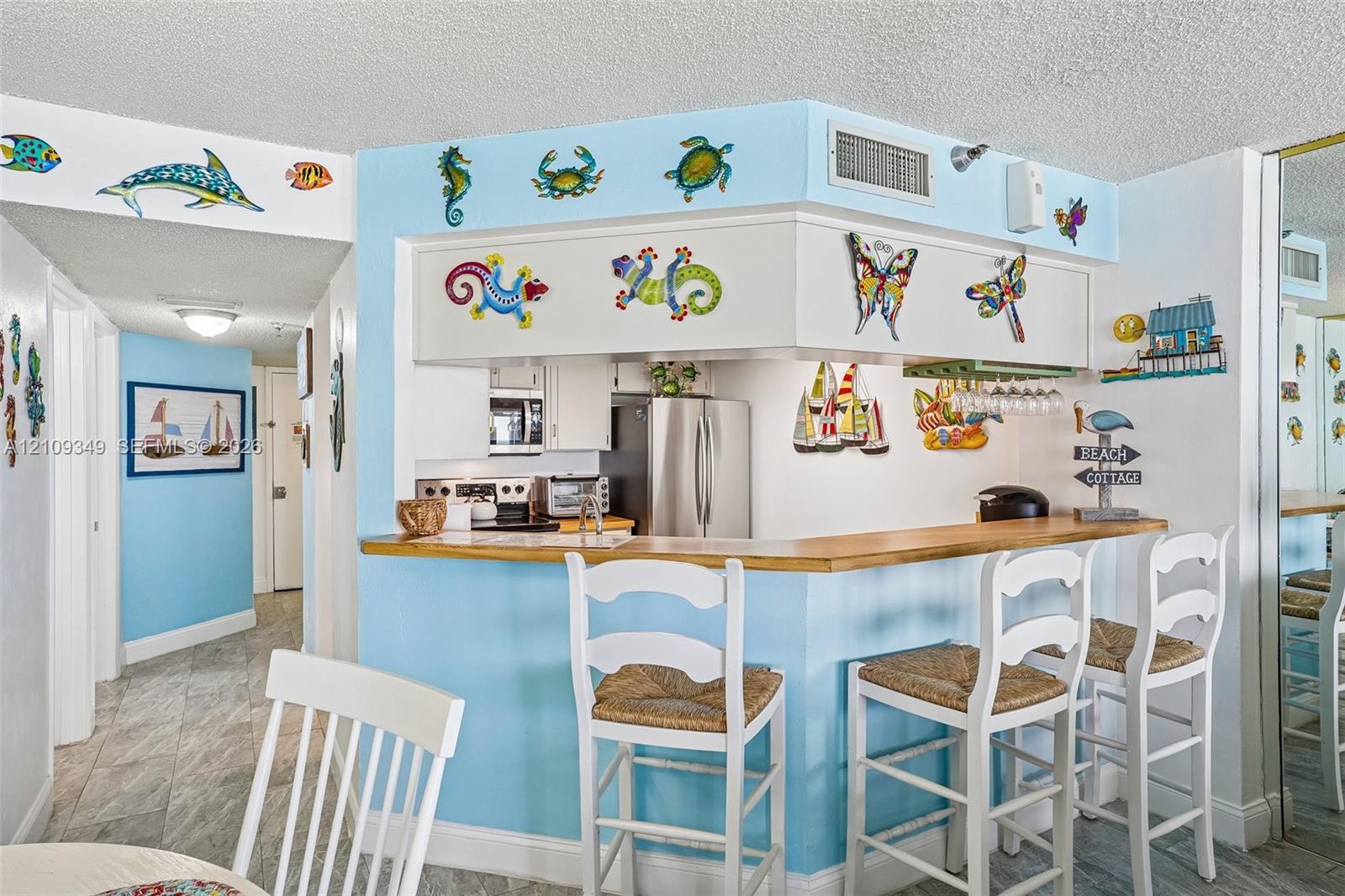Pass-through kitchen featuring stainless steel appliances, light-toned cabinetry, a wood-finish bar counter, and tile flooring