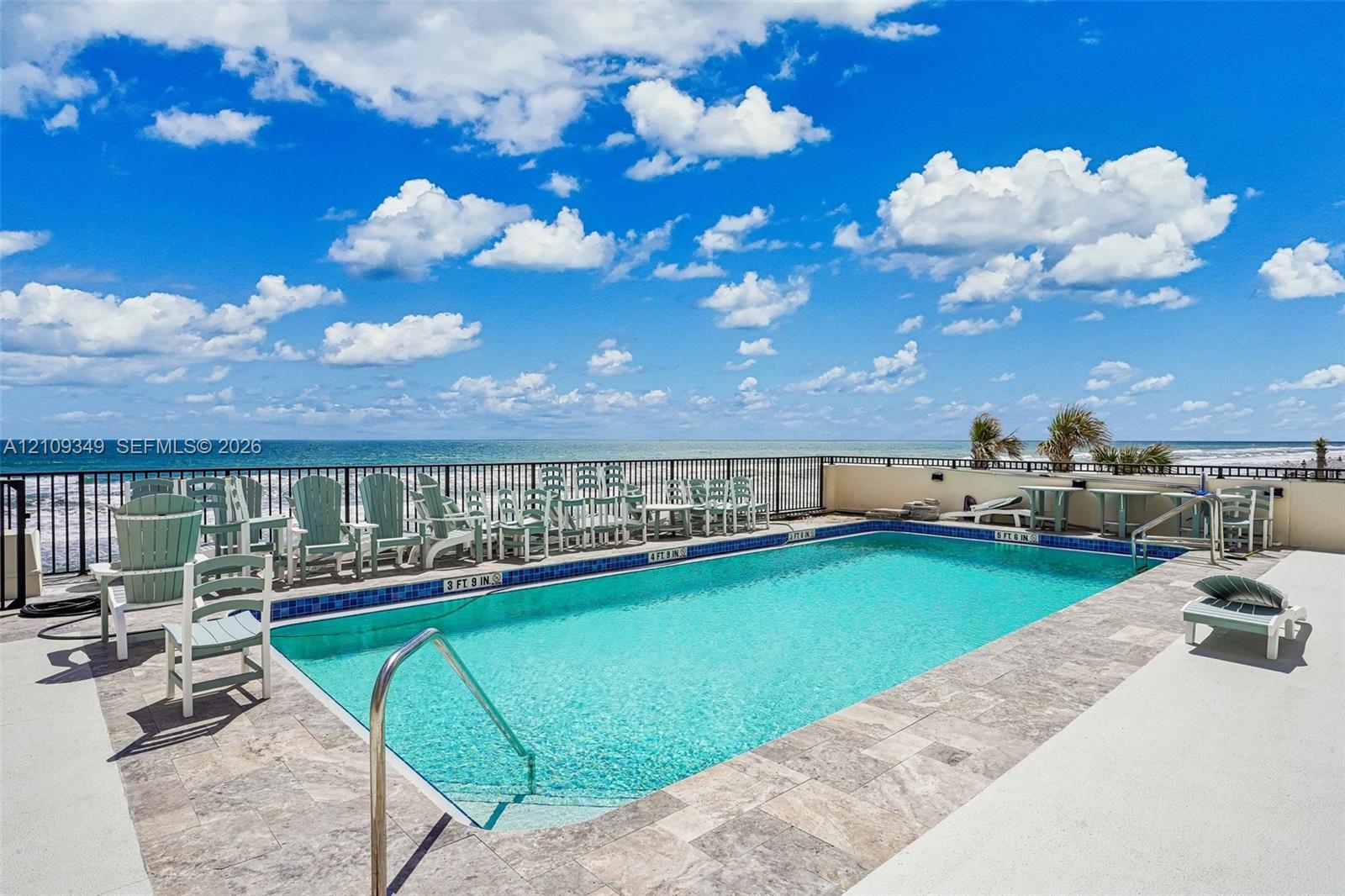 Swimming pool featuring stone-tile coping, metal perimeter fencing, and a metallic handrail