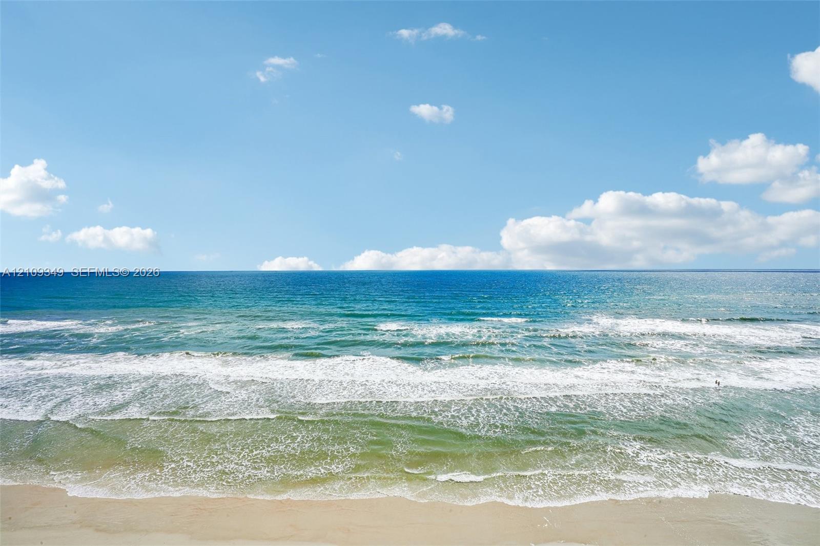 Sandy beach shoreline meeting the ocean with rolling surf and a clear sky horizon