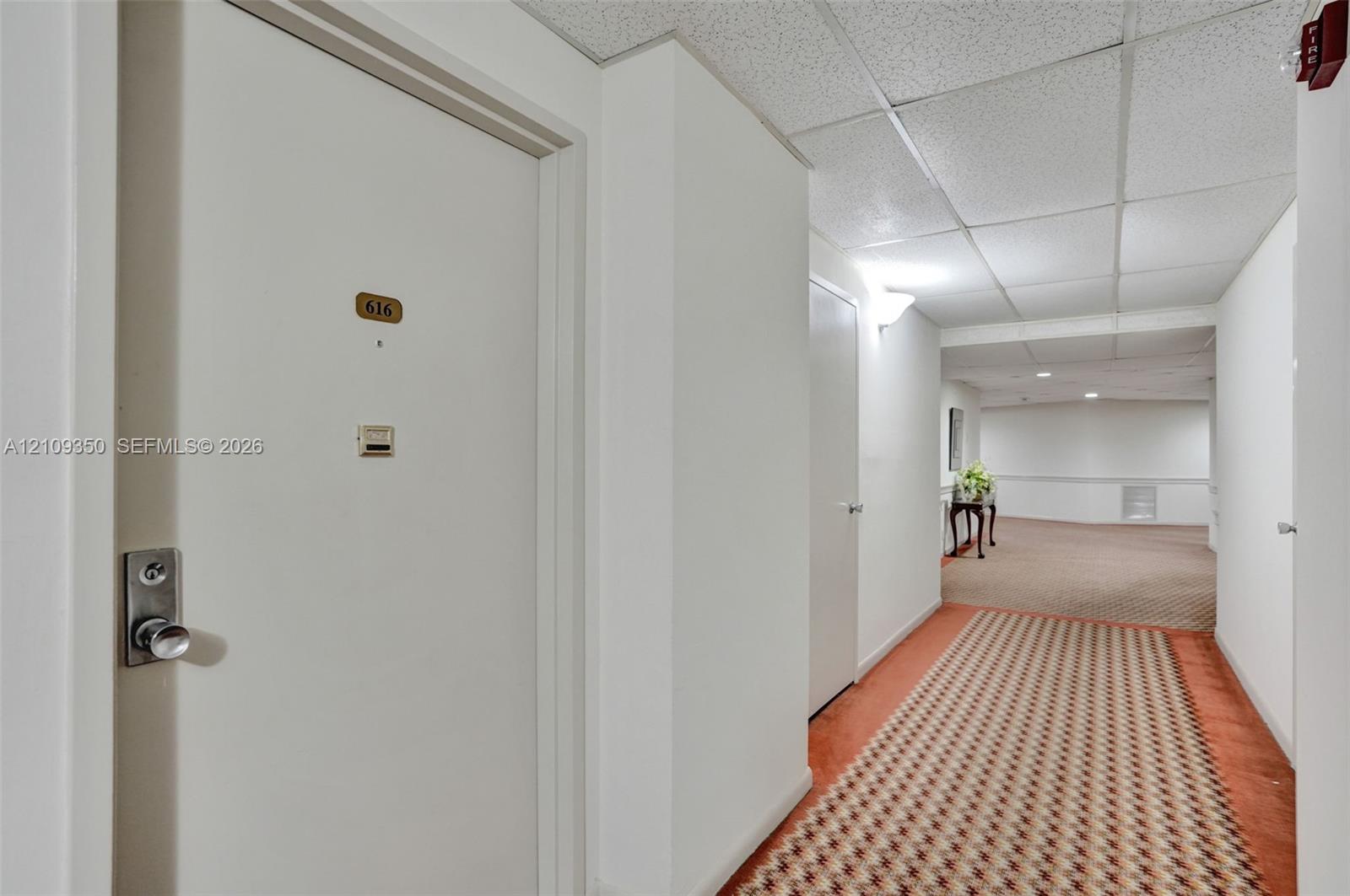 Hallway featuring patterned wall-to-wall carpeting, white interior doors, and a drop ceiling with integrated lighting