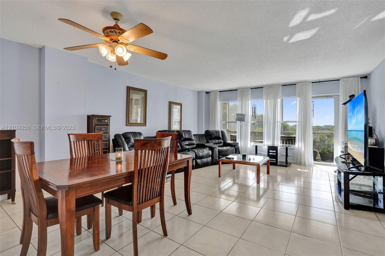 Neutral-toned tile flooring, oversized windows, light-filled interior, and a ceiling-mounted light fixture with fan