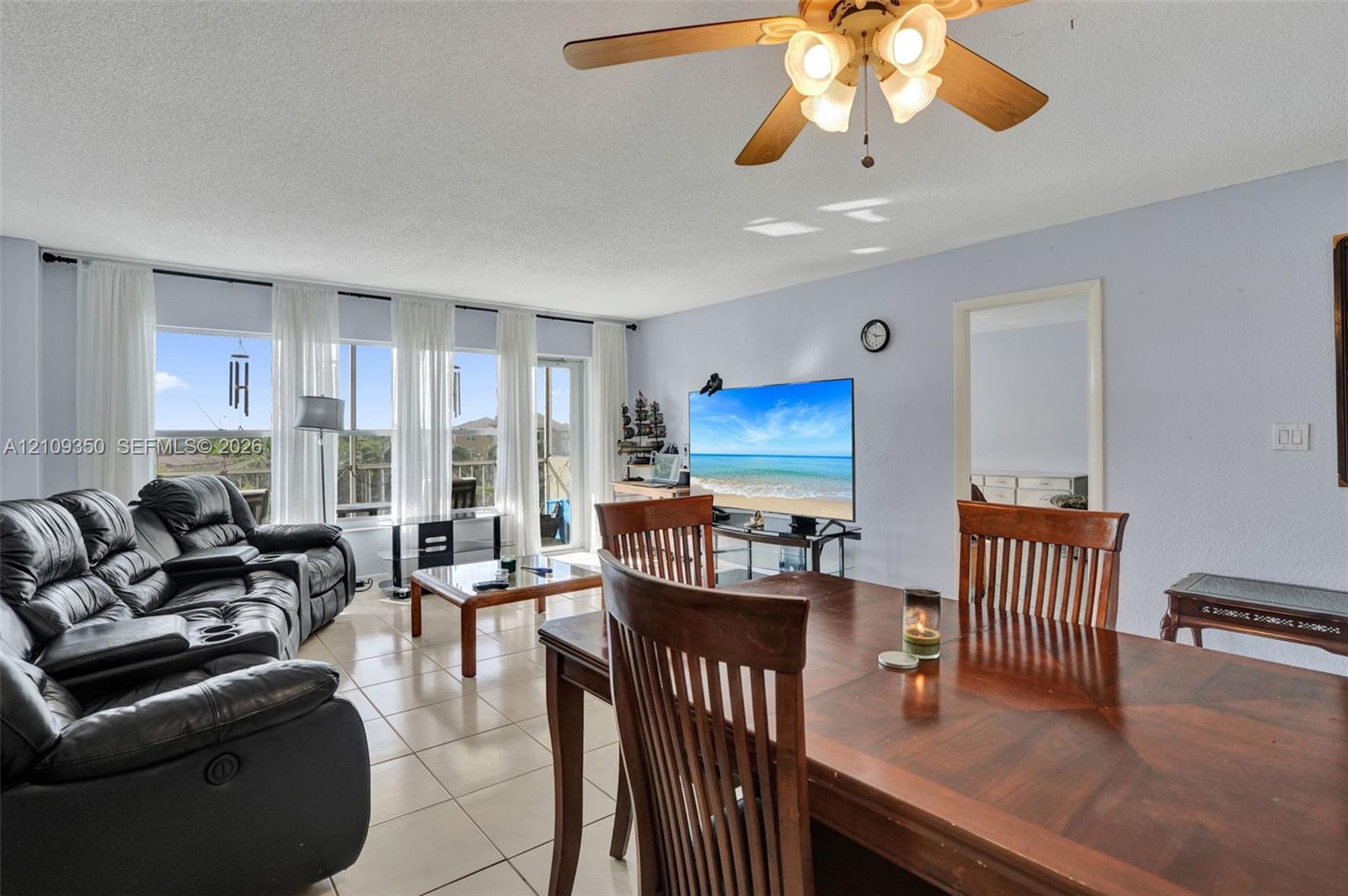 Living area featuring large-format ceramic tile flooring, a multi-light ceiling fan, and a floor-to-ceiling glass wall with access to an exterior space