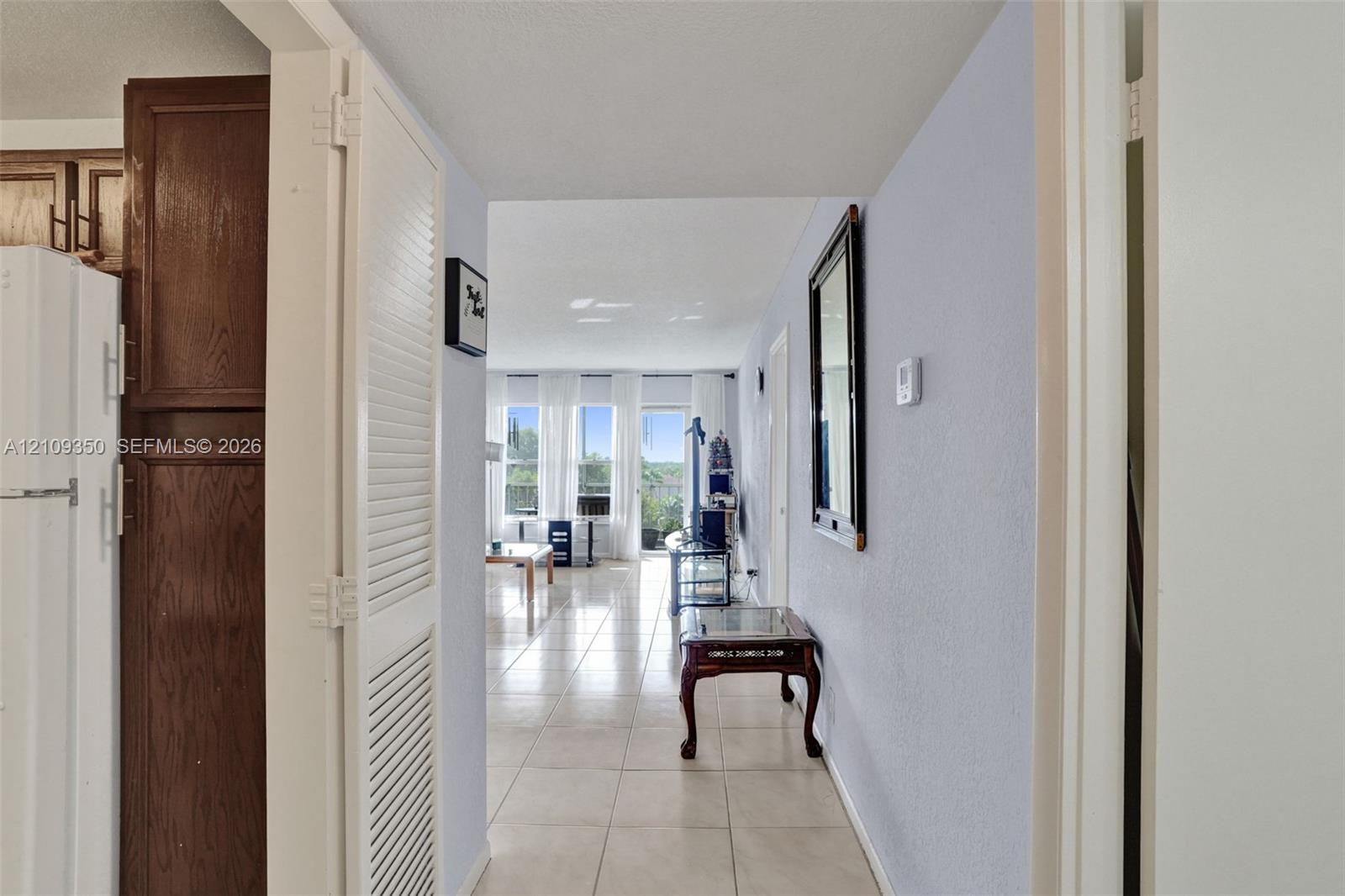 Interior hallway featuring large-format tile flooring, white louvered-door closet, and dark wood-finish cabinetry