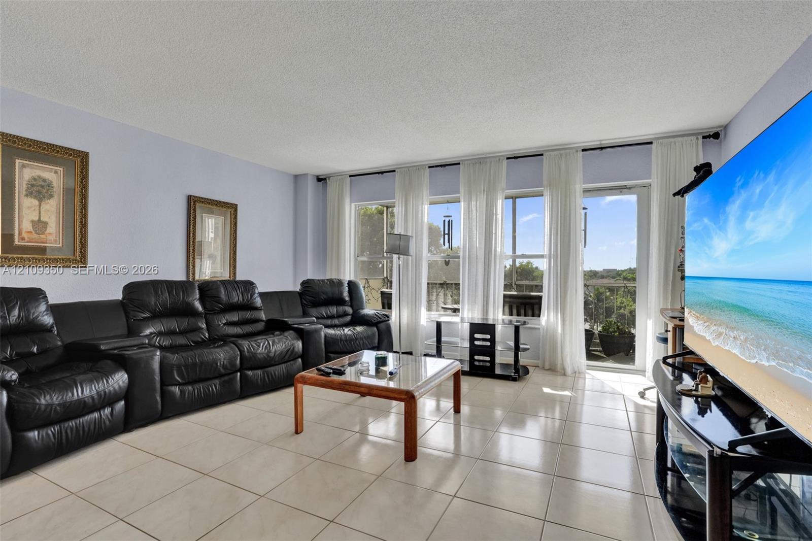 Living area featuring large-format ceramic tile flooring, floor-to-ceiling windows, and sliding glass door access to a balcony
