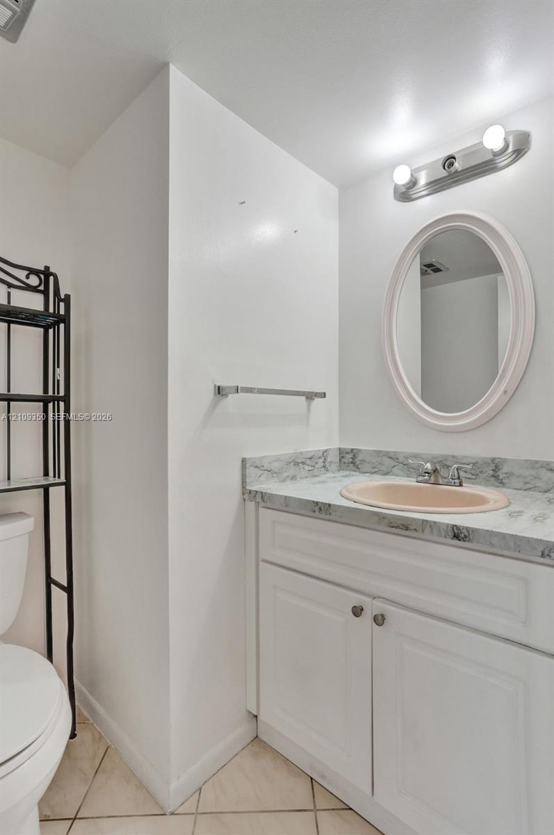 Bathroom vanity featuring a stone-patterned countertop, integrated oval sink, white shaker-style cabinetry, and an oval wall-mounted mirror
