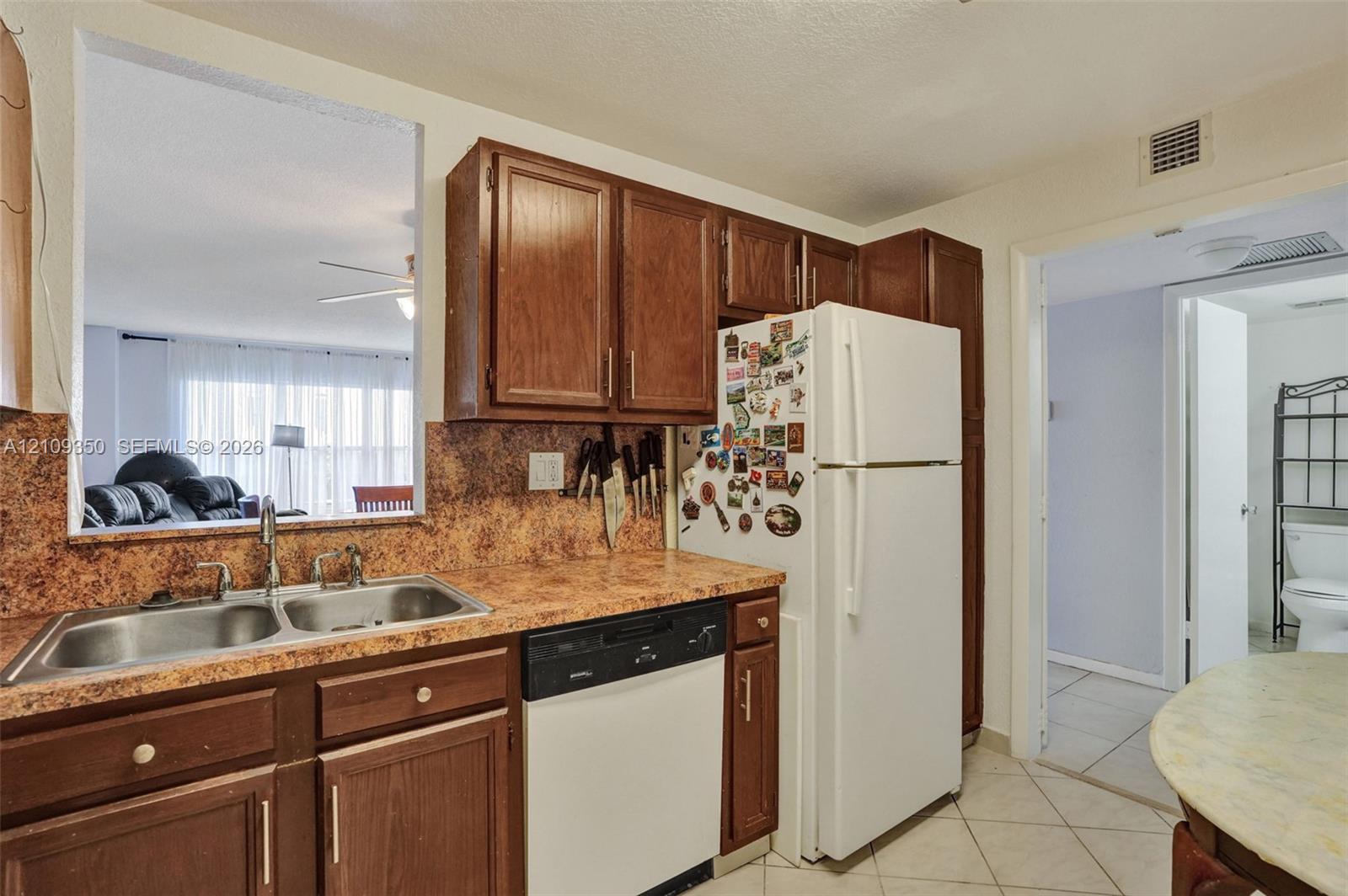 Kitchen featuring dark wood cabinetry, laminate countertops with a stone-finish pattern, a double-basin stainless steel sink, and a built-in dishwasher