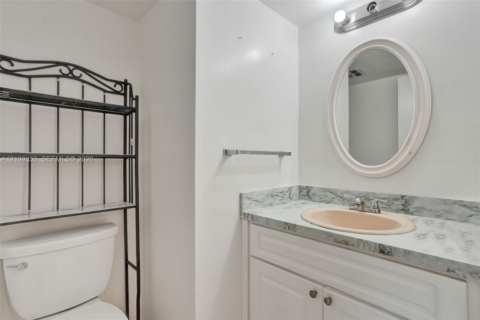Vanity featuring a stone-patterned countertop, integrated oval sink, chrome dual-handle faucet, white cabinetry, and an oval mirror with overhead lighting