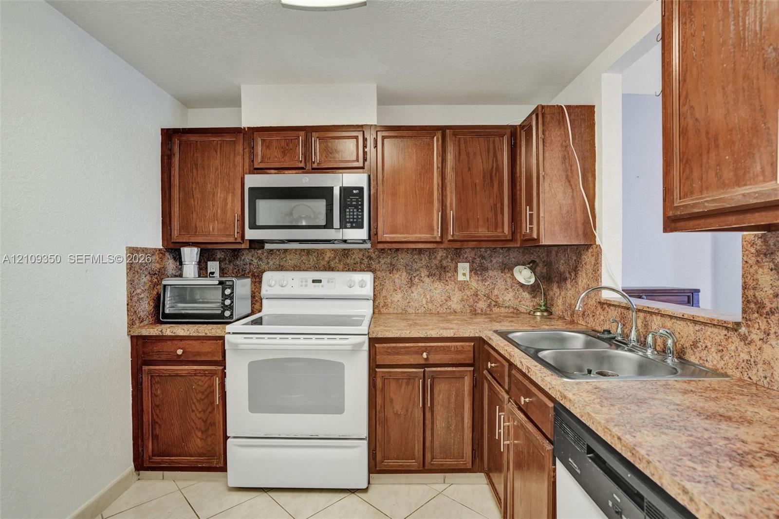 Kitchen featuring stained wood cabinetry, stone-finish countertops, tile flooring, and integrated stainless steel appliances including a range and microwave