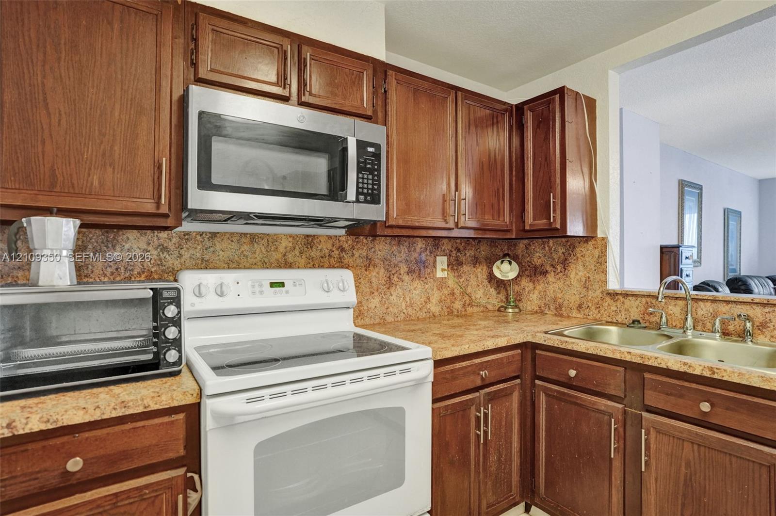 Kitchen featuring stained wood cabinetry, stone-patterned laminate countertops, double-basin stainless steel sink, and built-in stainless steel microwave